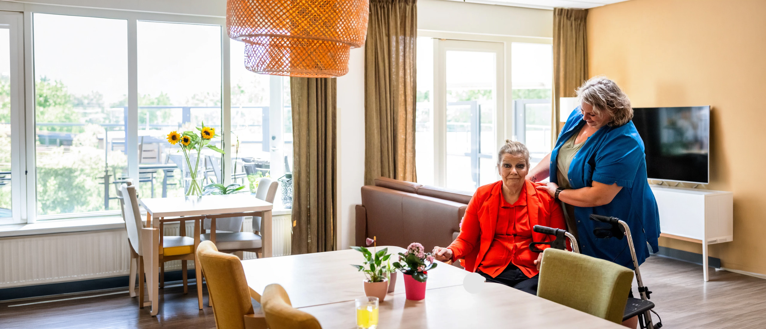 Zorgcollega van Topaz staat naast een bewoner aan tafel Zorgcollega van Topaz staat naast een bewoner aan tafel