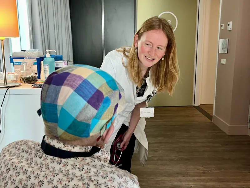 Zorgprofessional die vriendelijk met een bewoner praat tijdens een medisch bezoek.